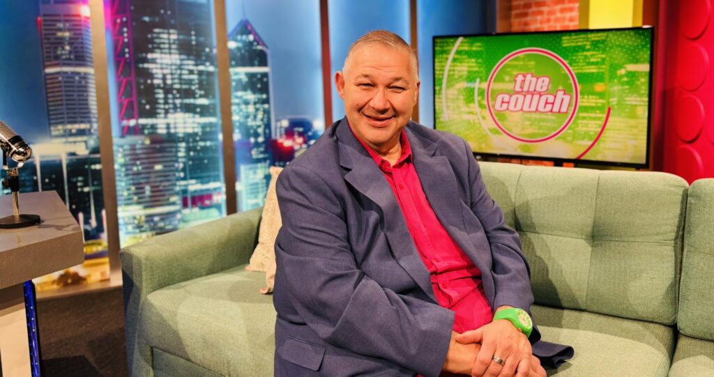 Smiling man seated on television talk show set
